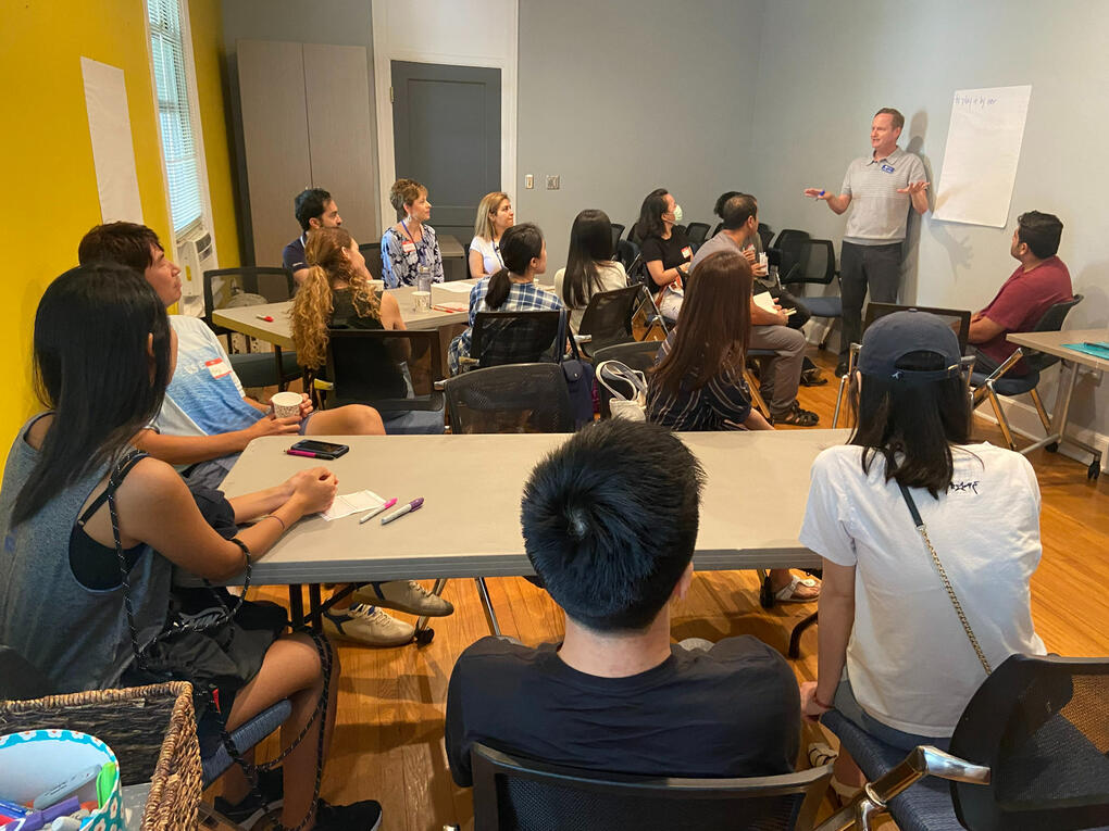 Groups sit at tables and listen to a speaker at the Summer English Conversations event hosted by the English for International Students program and International House